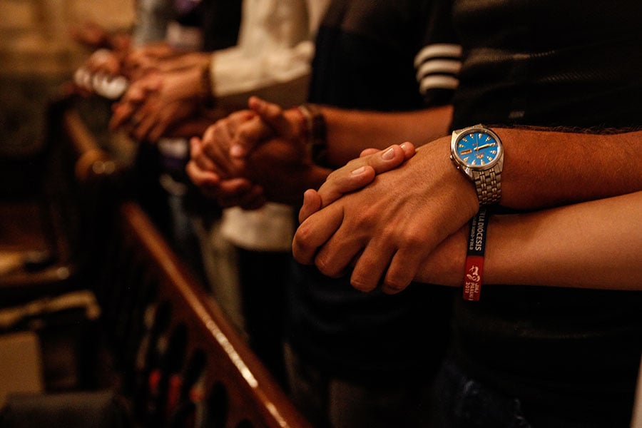 Young adults join hands in prayer during Mass
